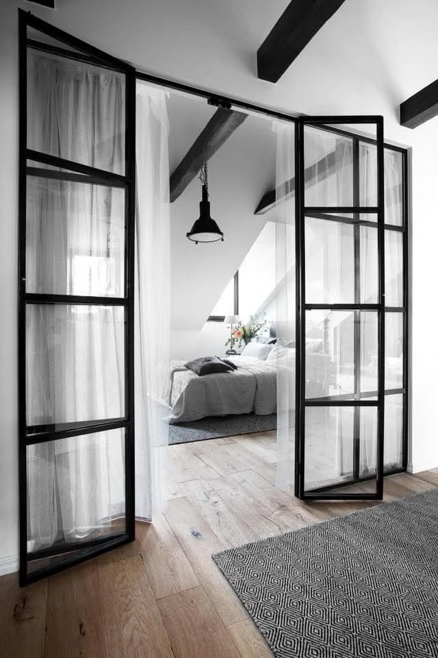 Schwarze Lofttür mit Metallrahmen und Glasfüllung in modernem Schlafzimmer mit hellem Holzboden