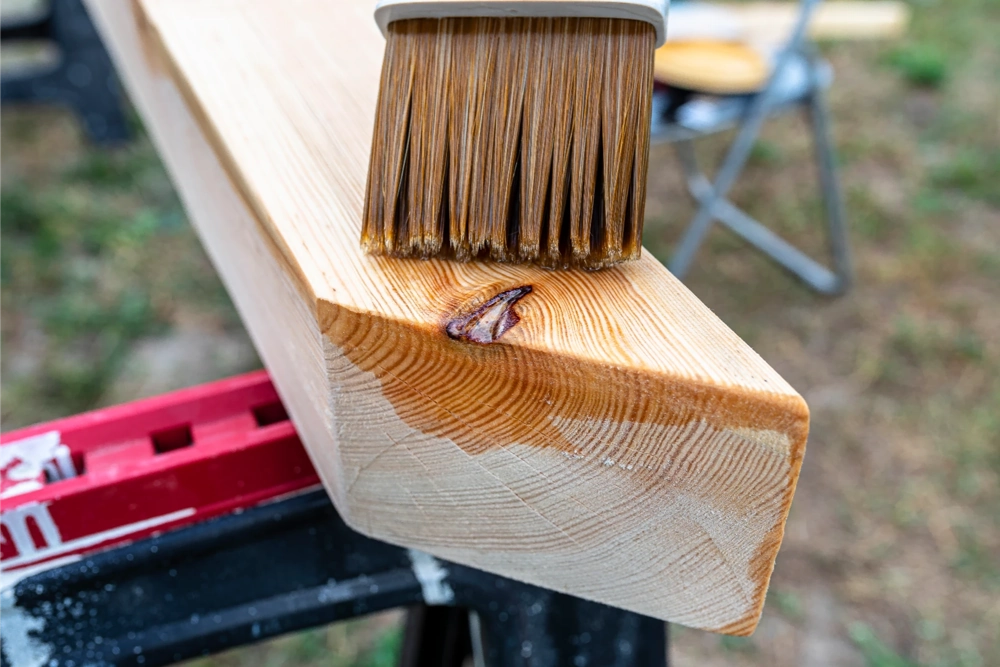 Holzimprägnierung: Pinselauftrag eines Schutzmittels auf geschliffenen Holzbalken im Freien